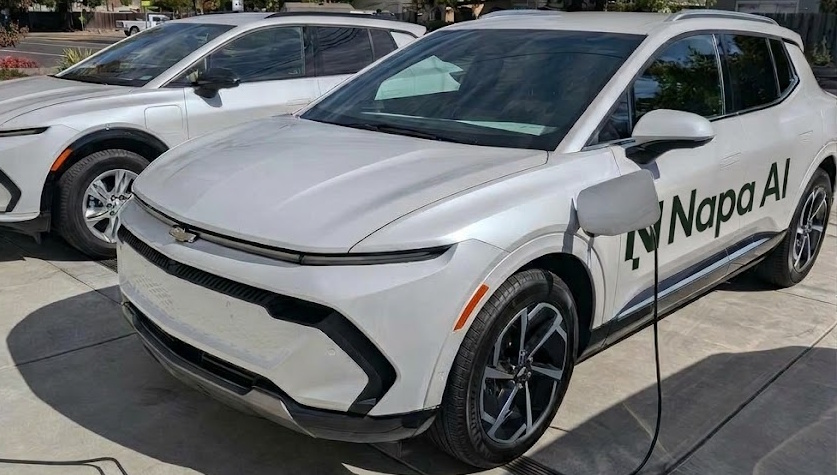 Two white Chevrolet electric SUVs, one plugged in to charge, with a Napa AI decal on the door